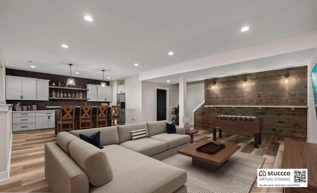 living room featuring bar area, wooden walls, and light hardwood / wood-style flooring