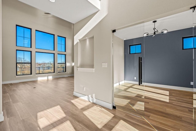 spare room featuring a notable chandelier, light hardwood / wood-style flooring, and a high ceiling