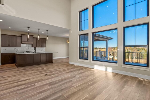 kitchen featuring light wood-type flooring, a kitchen island with sink, decorative light fixtures, dark brown cabinets, and decorative backsplash