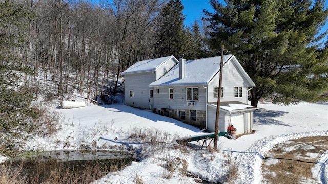 snow covered property with a chimney and an attached garage