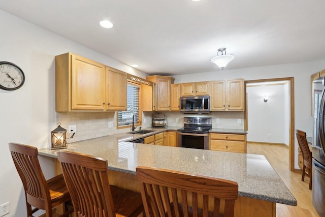 kitchen with appliances with stainless steel finishes, light brown cabinets, a sink, a peninsula, and a kitchen breakfast bar