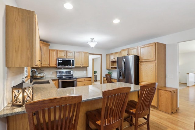 kitchen featuring appliances with stainless steel finishes, light stone counters, a peninsula, light wood-style floors, and a sink