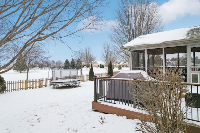 snowy yard with a trampoline, fence, a sunroom, and a hot tub