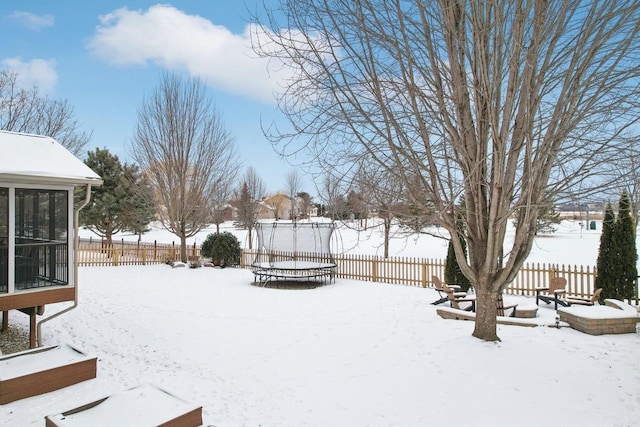 yard covered in snow with a trampoline and fence