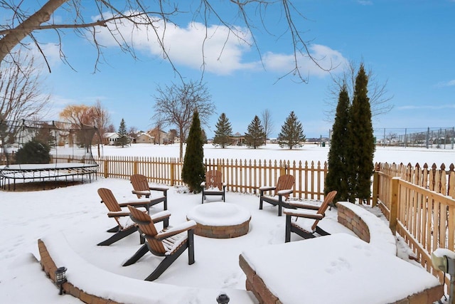 snow covered patio with a trampoline, fence, and a fire pit