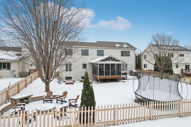 snow covered rear of property featuring fence private yard and a sunroom