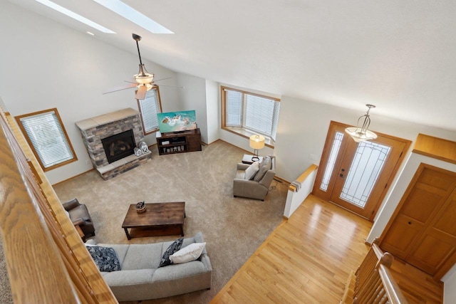 living room with carpet floors, a fireplace, wood finished floors, a ceiling fan, and lofted ceiling with skylight