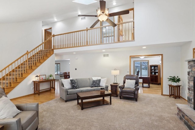 living room featuring light carpet, a skylight, visible vents, stairway, and a fireplace