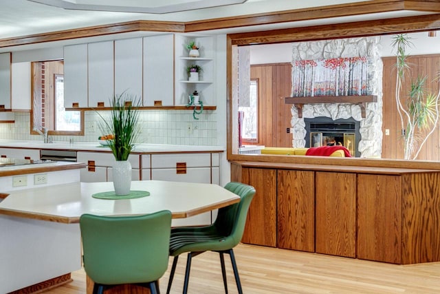 kitchen with a stone fireplace, light wood-type flooring, white cabinets, and backsplash