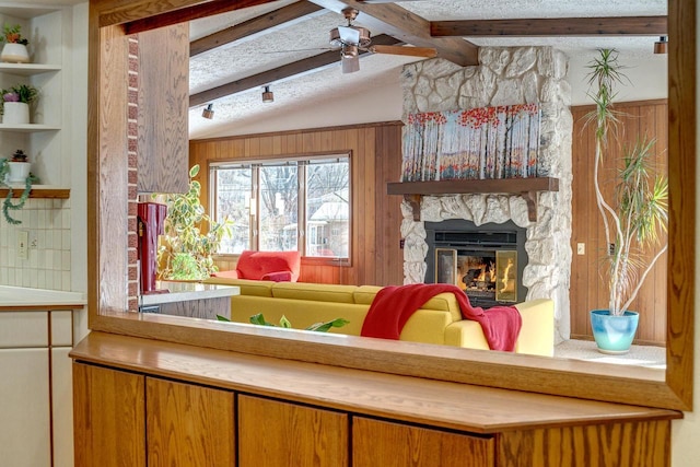 living room featuring vaulted ceiling with beams, built in shelves, a textured ceiling, ceiling fan, and a fireplace