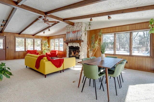 carpeted dining area featuring a stone fireplace, vaulted ceiling with beams, a textured ceiling, and wooden walls