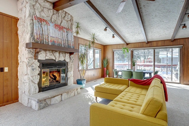 living room with carpet, a fireplace, wood walls, vaulted ceiling with beams, and a textured ceiling