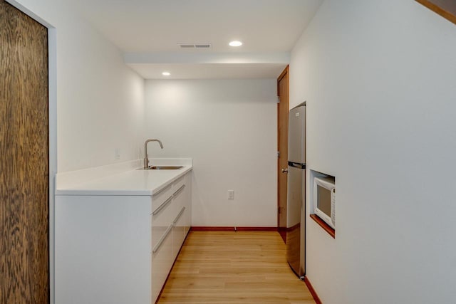 kitchen with white cabinets, light hardwood / wood-style floors, sink, and stainless steel refrigerator