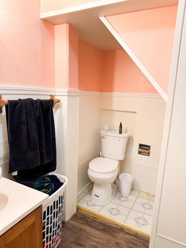 half bath featuring wainscoting, vanity, toilet, and wood finished floors