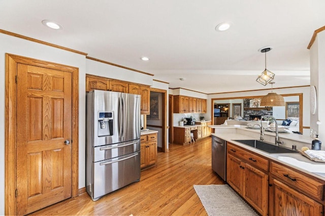 kitchen featuring appliances with stainless steel finishes, light hardwood / wood-style flooring, pendant lighting, a fireplace, and sink