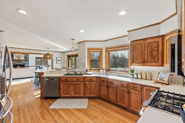 kitchen with appliances with stainless steel finishes, hanging light fixtures, a fireplace, sink, and kitchen peninsula