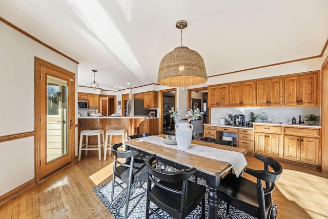 kitchen featuring light hardwood / wood-style flooring, a breakfast bar, crown molding, stainless steel fridge, and hanging light fixtures