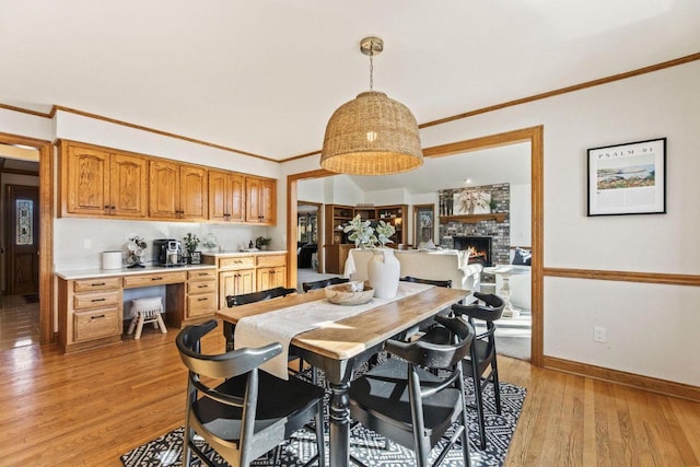 dining room with light hardwood / wood-style floors, crown molding, a stone fireplace, and built in desk