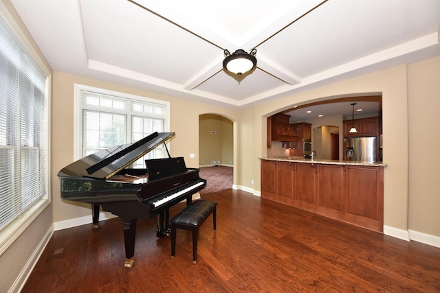 sitting room featuring dark wood-style floors, baseboards, arched walkways, and a tray ceiling