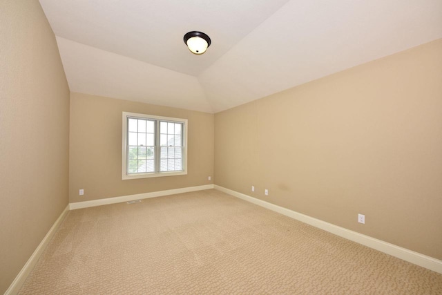 carpeted empty room featuring vaulted ceiling and baseboards