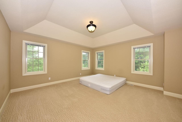 unfurnished bedroom with a tray ceiling, multiple windows, and baseboards