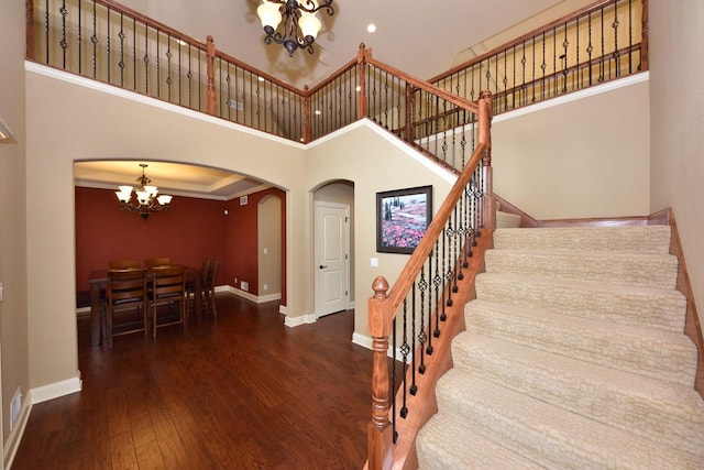 staircase featuring a chandelier, arched walkways, wood finished floors, a towering ceiling, and baseboards