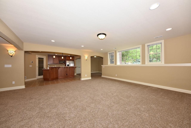 unfurnished living room featuring baseboards, visible vents, arched walkways, light colored carpet, and recessed lighting