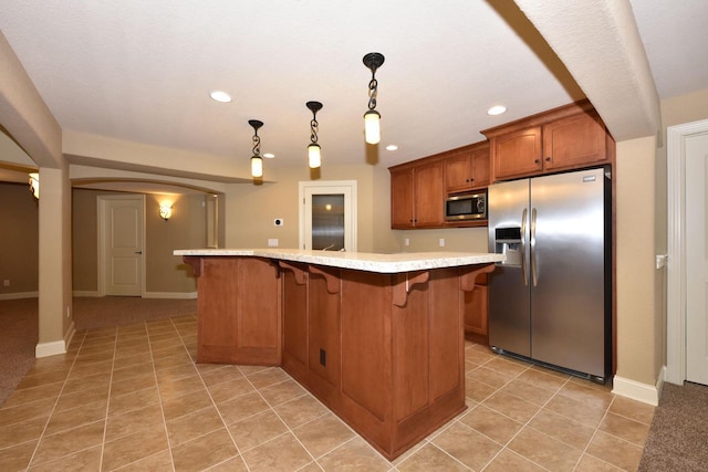 kitchen featuring appliances with stainless steel finishes, brown cabinets, hanging light fixtures, light countertops, and light tile patterned flooring