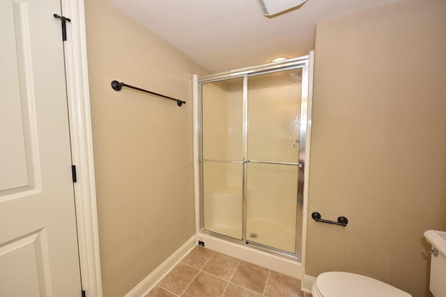 bathroom with a stall shower, baseboards, toilet, tile patterned flooring, and a textured ceiling