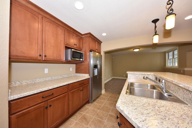 kitchen with pendant lighting, brown cabinets, light tile patterned floors, stainless steel appliances, and a sink