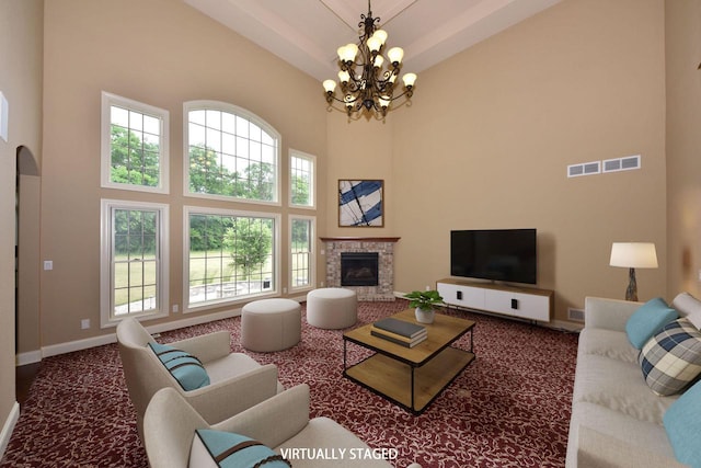 carpeted living room featuring a fireplace, a notable chandelier, visible vents, a towering ceiling, and baseboards