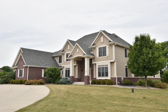 craftsman-style house featuring a shingled roof, a front yard, and brick siding