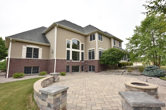 rear view of house with an outdoor fire pit, a patio area, brick siding, and a shingled roof