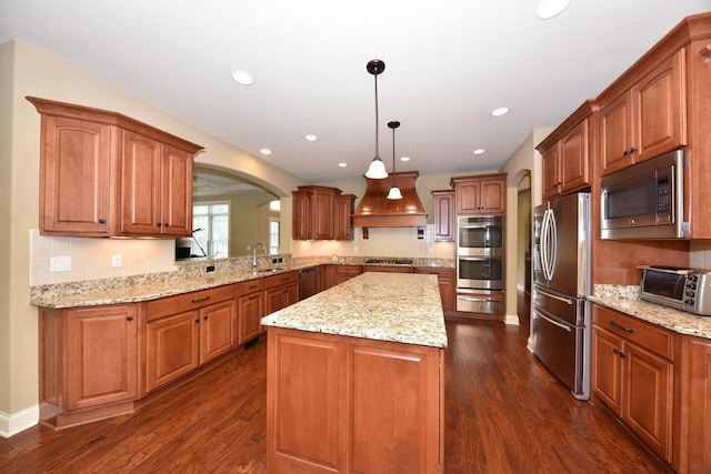 kitchen with decorative light fixtures, a warming drawer, appliances with stainless steel finishes, a sink, and premium range hood