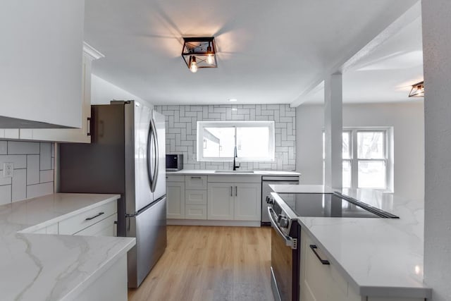 kitchen with appliances with stainless steel finishes, light stone counters, white cabinets, backsplash, and sink