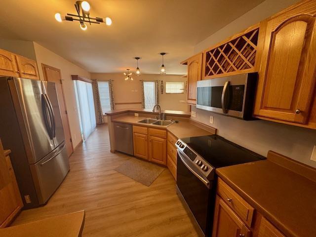 kitchen featuring appliances with stainless steel finishes, sink, a notable chandelier, light hardwood / wood-style floors, and hanging light fixtures