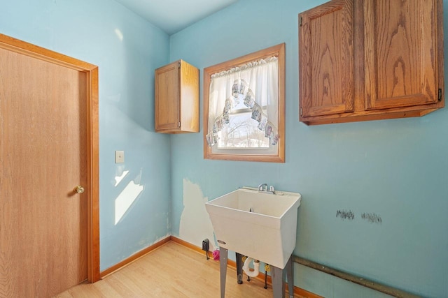 clothes washing area featuring sink, cabinets, and light hardwood / wood-style floors