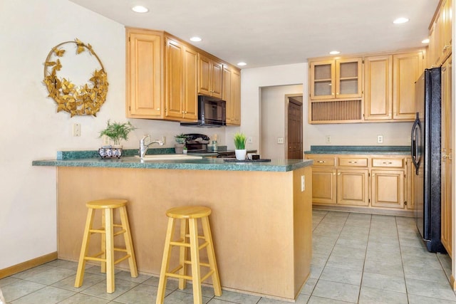 kitchen with light brown cabinetry, a breakfast bar area, black appliances, sink, and kitchen peninsula