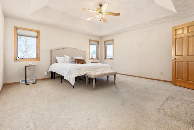 carpeted bedroom with multiple windows, ceiling fan, and a raised ceiling