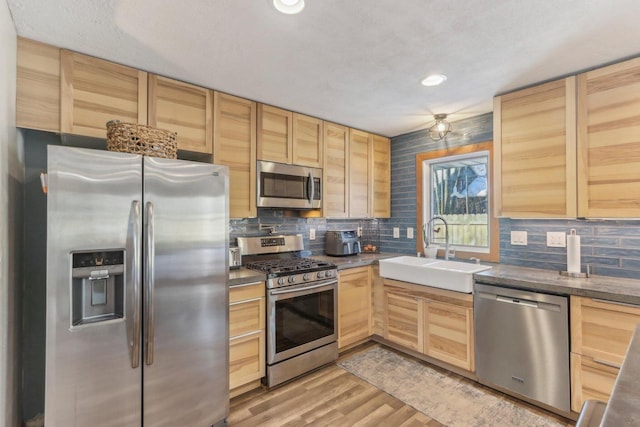 kitchen featuring light brown cabinetry, stainless steel appliances, decorative backsplash, light wood-type flooring, and sink