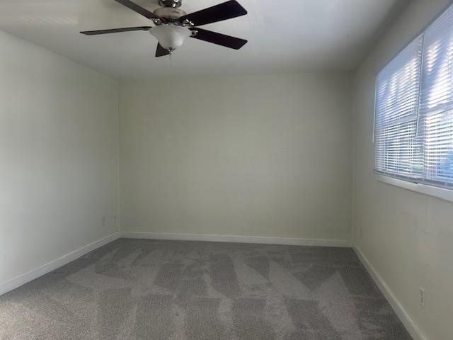 spare room featuring ceiling fan and dark colored carpet