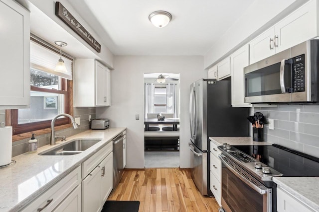 kitchen featuring appliances with stainless steel finishes, light wood-type flooring, backsplash, sink, and white cabinetry