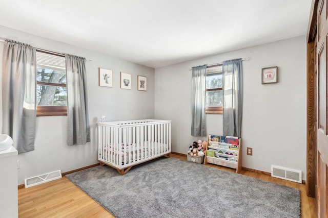 bedroom featuring a crib, multiple windows, and wood-type flooring