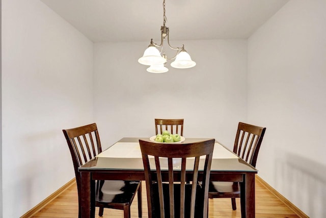 dining space featuring light wood finished floors, baseboards, and an inviting chandelier