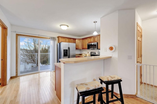 kitchen featuring light wood-style flooring, a peninsula, stainless steel appliances, light countertops, and a kitchen bar