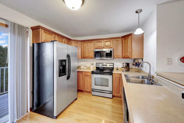 kitchen with decorative light fixtures, stainless steel appliances, light countertops, light wood-type flooring, and a sink