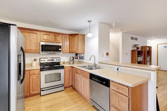 kitchen with stainless steel appliances, light countertops, hanging light fixtures, a sink, and a peninsula