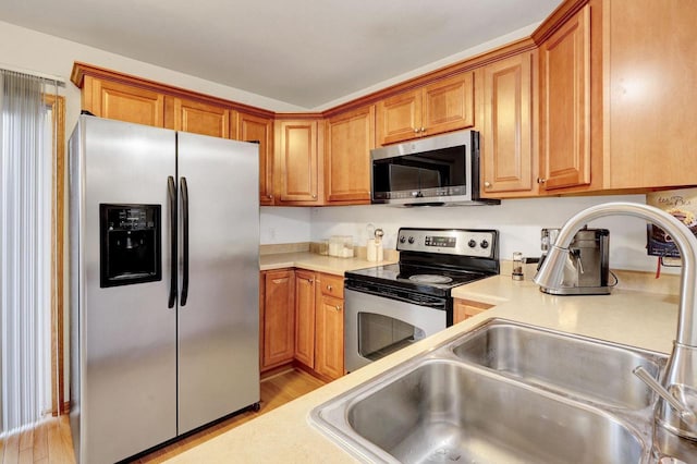 kitchen with stainless steel appliances, light countertops, brown cabinetry, a sink, and light wood-type flooring