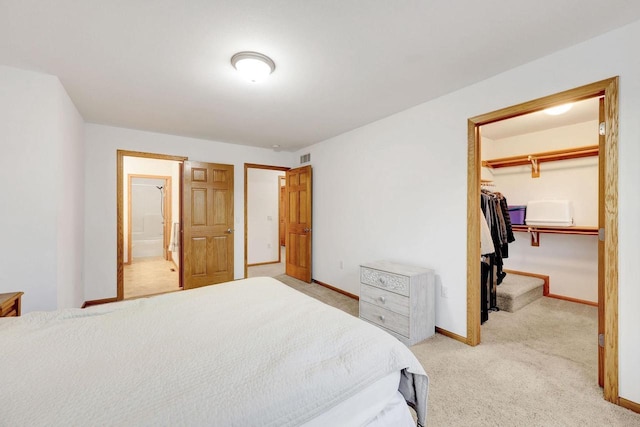 bedroom featuring a walk in closet, a closet, light carpet, ensuite bath, and baseboards