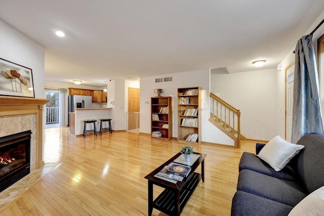 living room with a fireplace, visible vents, stairway, light wood-type flooring, and baseboards